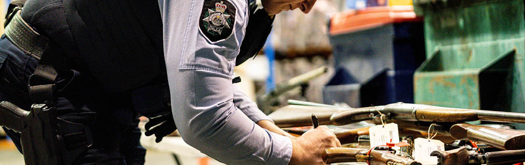 A police officer in uniform labelling guns on a table 