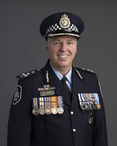 A forward facing portrait image of a male police commander wearing full uniform with police cap, epaulettes and ten medals fixed to the chest of his jacket.