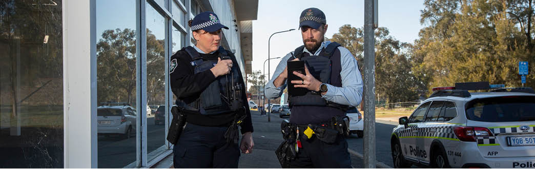 A picture of two officers in uniform one is on radio and one is writing on a note pad