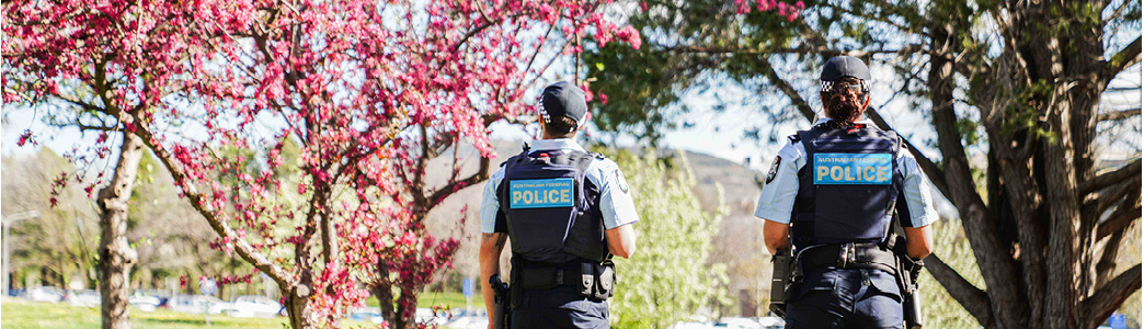 A picture of the back of two police officers with pink blossom trees in the background 