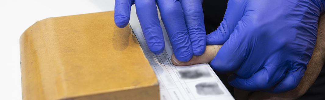 A hand guiding another hand through a fingerprinting process.