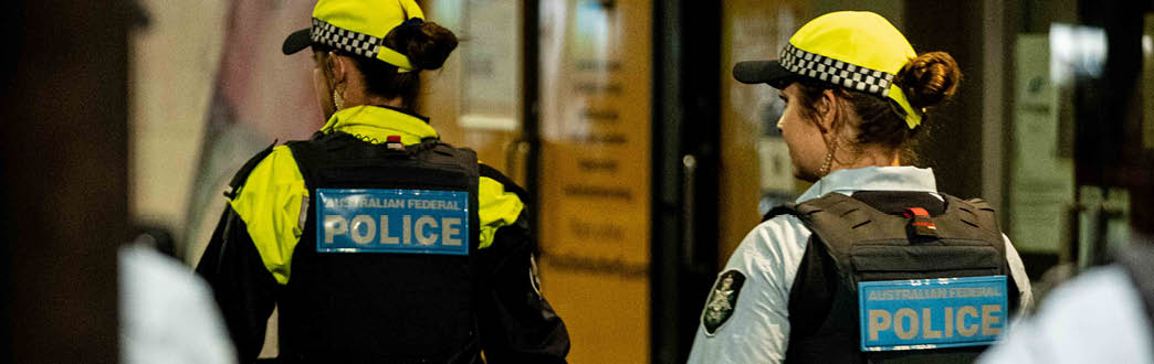 Three police officers in high visibility uniform walking through a park at night 