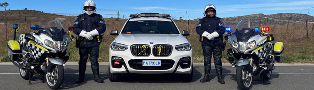 Two police officers standing in between a motorbike and police car 