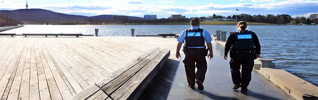 Picture of a male and female police officer walking along a board walk on the lake with thee carillion in the background.